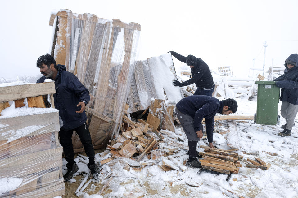 Migrants load firewood into garbage containers at the Lipa camp, outside Bihac, Bosnia, Friday, Jan. 8, 2021. A fresh spate of snowy and very cold winter weather on has brought more misery for hundreds of migrants who have been stuck for days in a burnt out camp in northwest Bosnia waiting for heating and other facilities. (AP Photo/Kemal Softic)