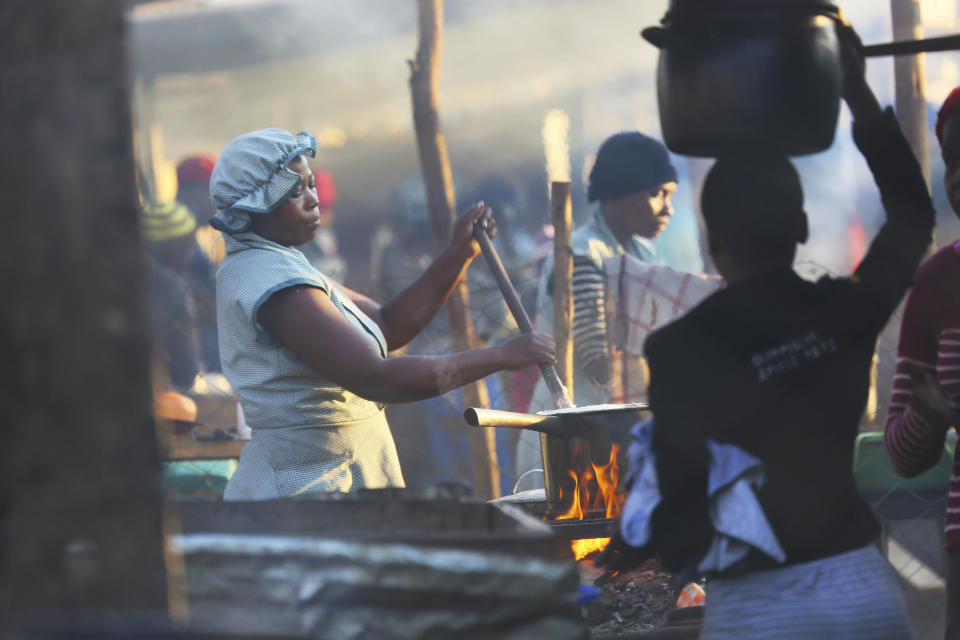 A woman prepares a meal in a busy market in Harare, Thursday, Aug, 8, 2019. Many Zimbabweans who cheered the downfall of longtime leader Robert Mugabe two years ago now find the country's economy worse than before.(AP Photo/Tsvangirayi Mukwazhi)