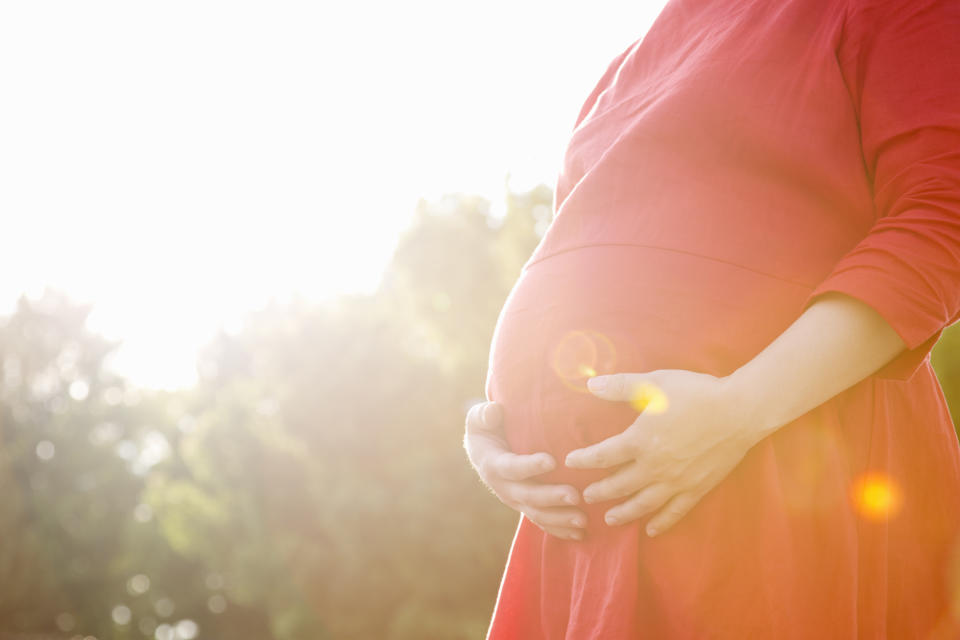 Eine schwangere Frau hält ihren Babybauch in einem Park im Sonnenschein