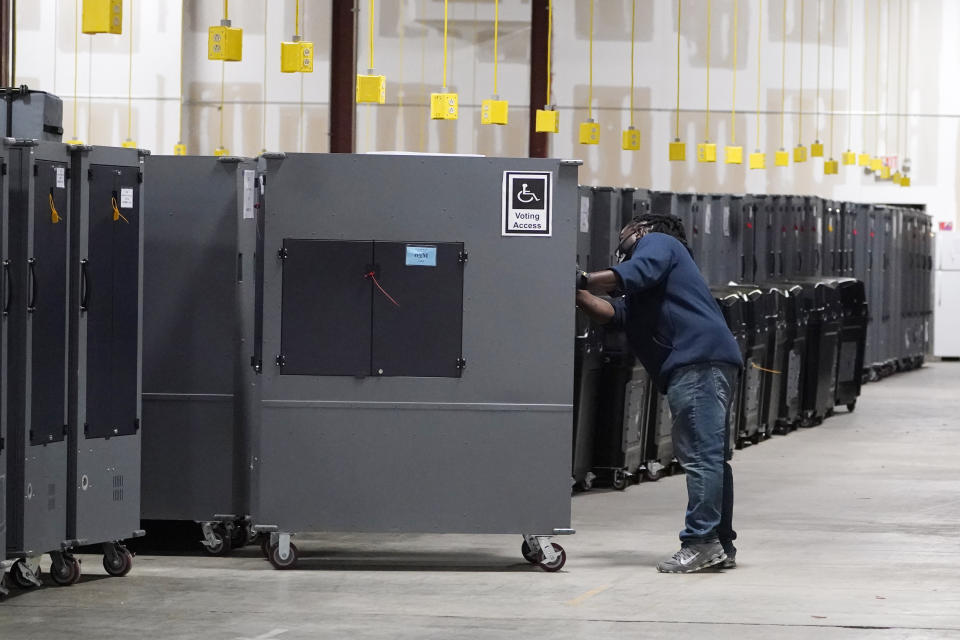 FILE - A worker returns voting machines to storage at the Fulton County Election preparation Center on Nov. 4, 2020 in Atlanta, Ga. A group of state election officials is urging the nation's cybersecurity agency to revise a draft rule that would require election offices to disclose suspected cyber attacks to the federal government, casting the mandate as too burdensome on overworked local officials. (AP Photo/John Bazemore, File)