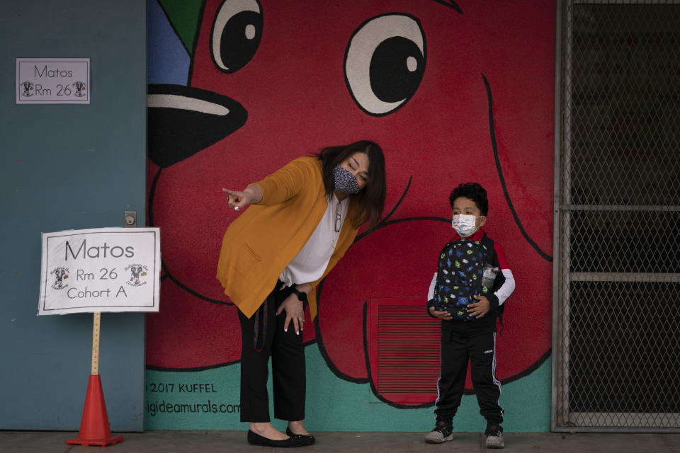 Kindergarten teacher Lilia Matos and her student Jesus Mendez stand outside their classroom on the first day of in-person learning at Heliotrope Avenue Elementary School in Maywood, Calif., Tuesday, April 13, 2021. More than a year after the pandemic forced all of California's schools to close classroom doors, some of the state's largest school districts are slowly beginning to reopen this week for in-person instruction. (AP Photo/Jae C. Hong)