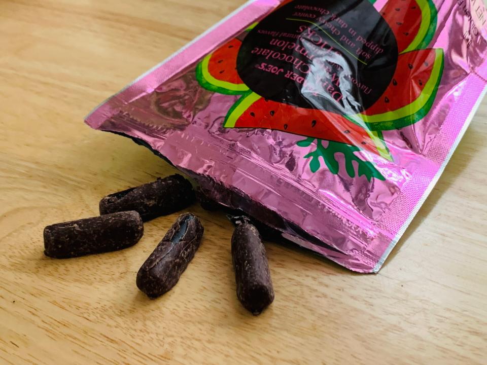 Trader joe's chocolate watermelon sticks spilling out of the pink packaging on a light wood table