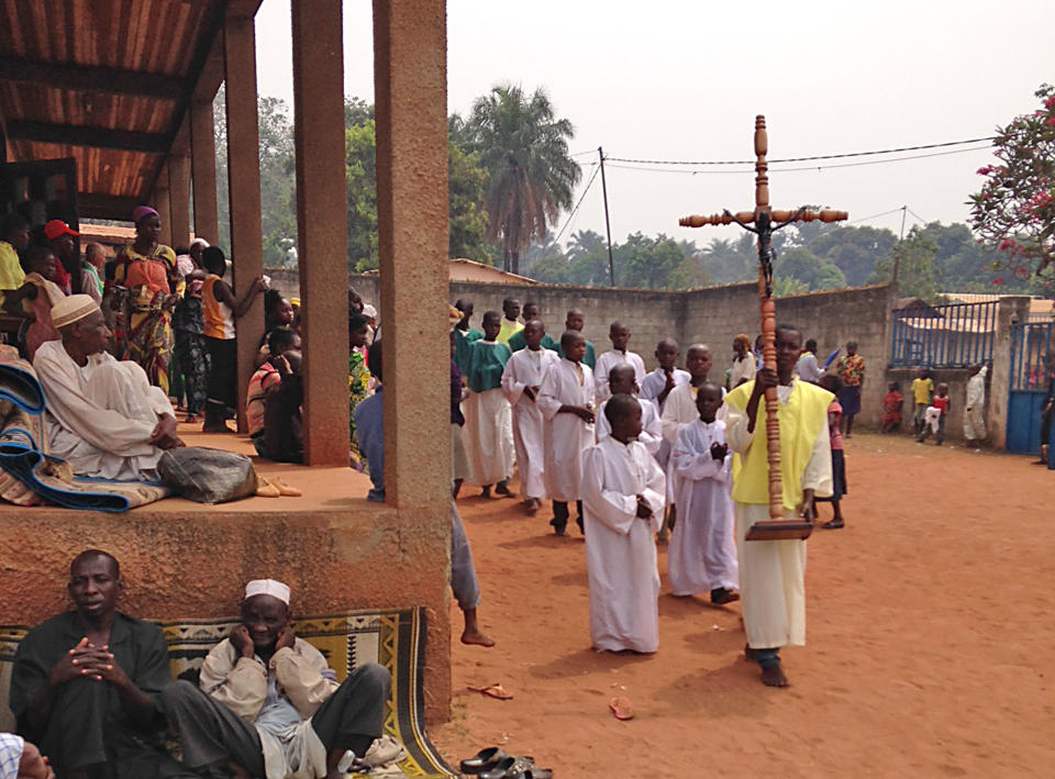 In this photo taken on Sunday, Feb. 23, 2014, Muslim men, left, seeking refuge in a Catholic church, look on as a Catholic church service takes place in Carnot a town 200 kilometers (125 miles) from the Cameroonian border, in, Central African Republic. The Christian militiamen knew hundreds of Muslims were hiding at the Catholic church and came with their ultimatum: Evict the families to face certain death or else the entire place would be burned to the ground. (AP Photo/Krista Larson)