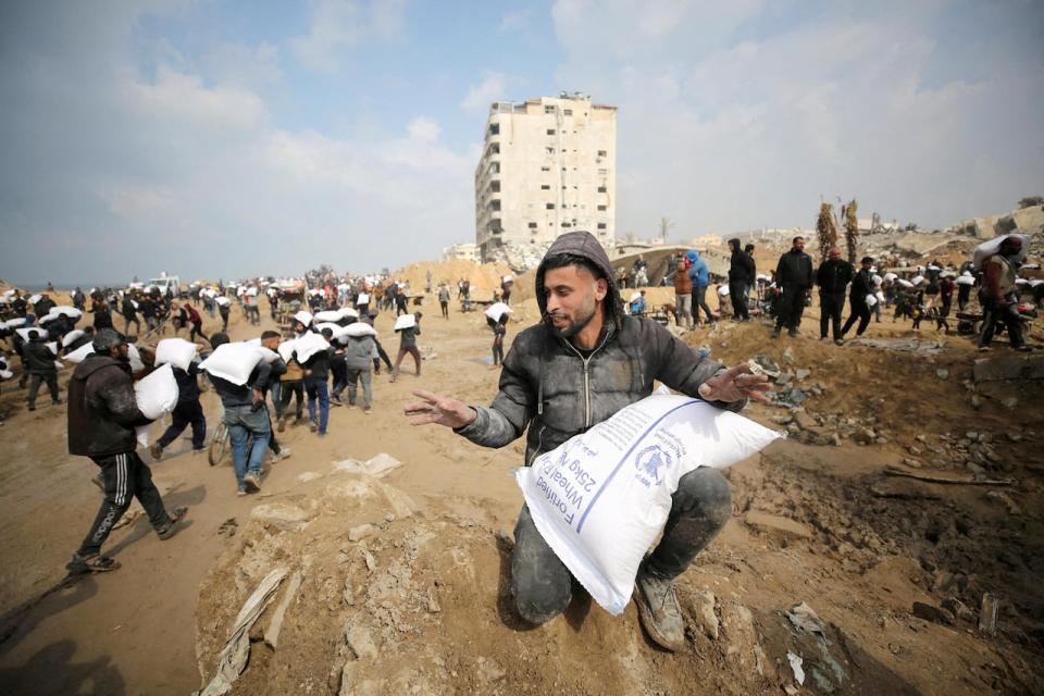 Palestinians carry bags of flour they grabbed from an aid truck near an Israeli checkpoint on Feb. 19. A non-binding motion calls on Canada's government to take a number of actions in response to the Israel-Hamas war, including that it should 'officially recognize the State of Palestine.'  (Kosay Al Nemer/Reuters - image credit)