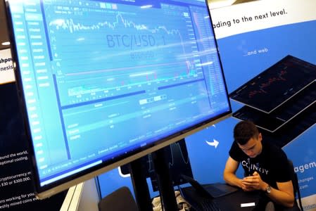 FILE PHOTO: FILE PHOTO: A man works beneath a display showing the market price of Bitcoin on the floor of the Consensus 2018 blockchain technology conference in New York City
