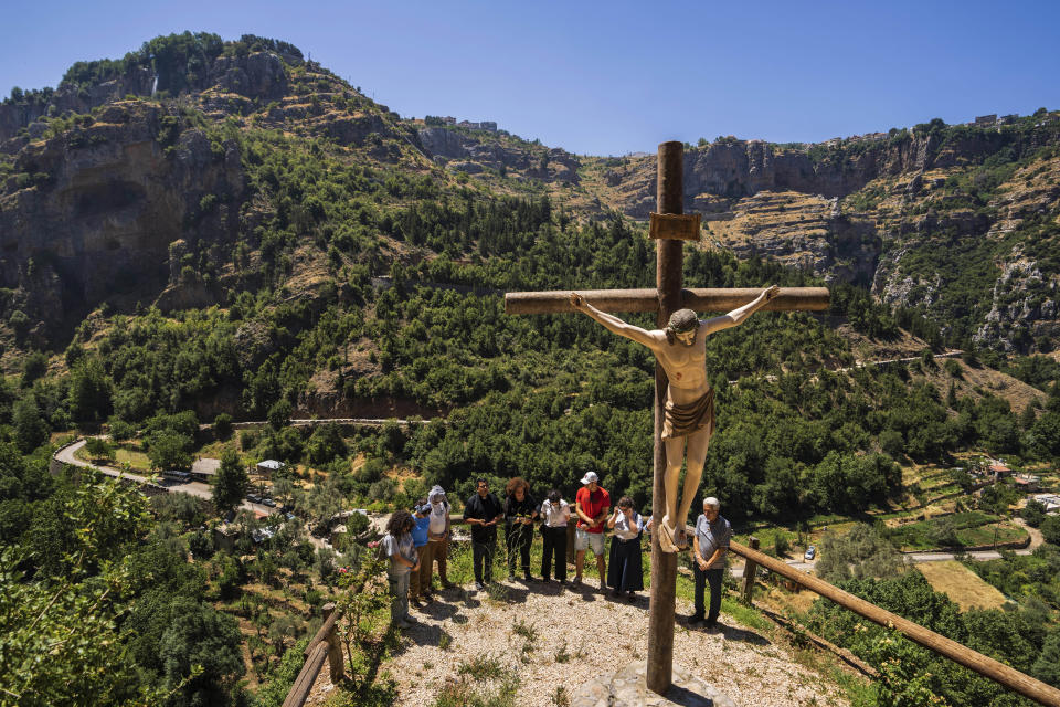 Lebanese priest Hani Tawk, center, prays with French tourists and his family next to a cross with a statue of a crucified Jesus Christ outside the Saint Elisha monastery in the Kadisha Valley, a holy site by Lebanon's Christians, in the northeast mountain town of Bcharre, Lebanon, Saturday, July 22, 2023. For Lebanon's Christians, the cedars are sacred, these tough evergreen trees that survive the mountain's harsh snowy winters. They point out with pride that Lebanon's cedars are mentioned 103 times in the Bible. (AP Photo/Hassan Ammar)