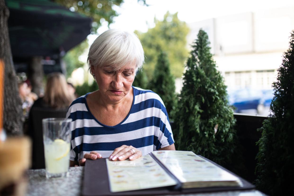 Gray hair woman sitting at cafe and looking at menu, choosing what to order, drinking lemonade