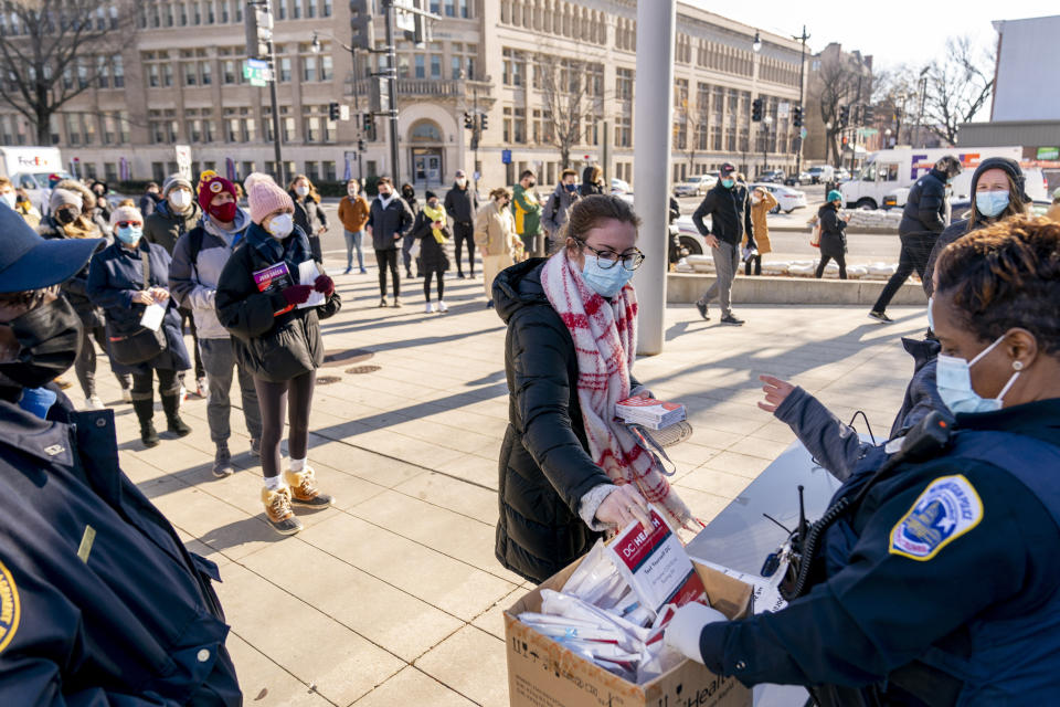 FILE - A woman receives at-home COVID-19 test kits after waiting in a long line that snakes multiple times around the Shaw Library in Washington, Dec. 22, 2021. The COVID-19 surge caused by the omicron variant means once-reliable indicators of the pandemic's progress are much less so, complicating how the media is able to tell the story. (AP Photo/Andrew Harnik, File)