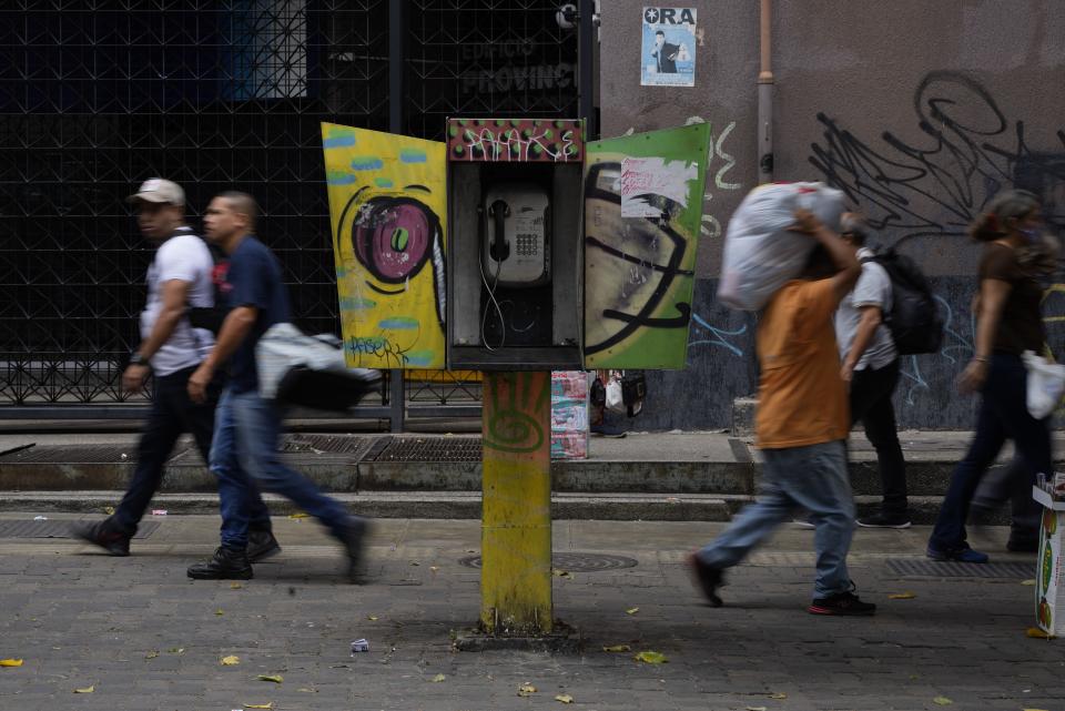 Pedestrians walk past an out of service National Telephone Company of Venezuela, CANTV, phone booth, in Caracas,Venezuela, Friday, May 13, 2022. A number of Venezuelan state-owned companies, including in the telecommunications sector, will sell up to 10% of their shares starting Monday. President Nicolas Maduro says the companies will be listed in the country's stock exchange and the sale is open to local and foreign investors. (AP Photo/Ariana Cubillos)