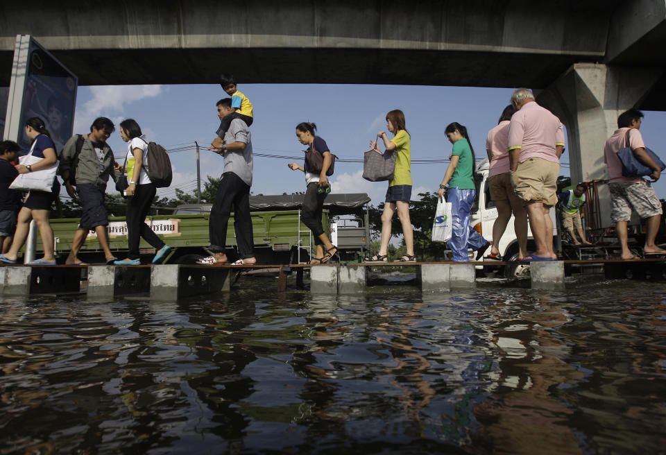 FILE - In this Thursday, Nov. 10, 2011 file photo, pedestrians use an elevated makeshift walkway to avoid the floodwaters in Bangkok, Thailand. The year 2011 brought a record heat wave to Texas, massive floods in Bangkok and an unusually warm November in England. How much has global warming boosted the chances of events like that? Quite a lot in Texas and England, but apparently not at all in Bangkok, according to new analyses released Tuesday, July 10, 2012. It found no sign that climate change played a role in that event, noting that the amount of rainfall was not very unusual. The scale of the flooding was influenced more by factors like reservoir operation policies, researchers wrote. (AP Photo/Aaron Favila)