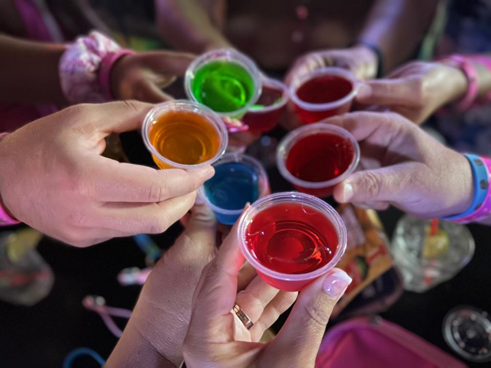 A photo of hands holding multi-colored Jello shots