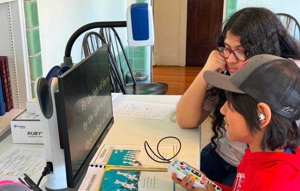 Juan Juarez Reyes, foreground, and his older sister Selena Juarez Reyes try out a portable desktop magnifier.