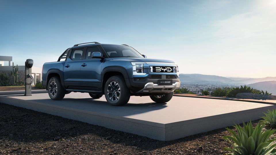 A blue BYD Shark hybrid pickup truck parked before an electric charger.