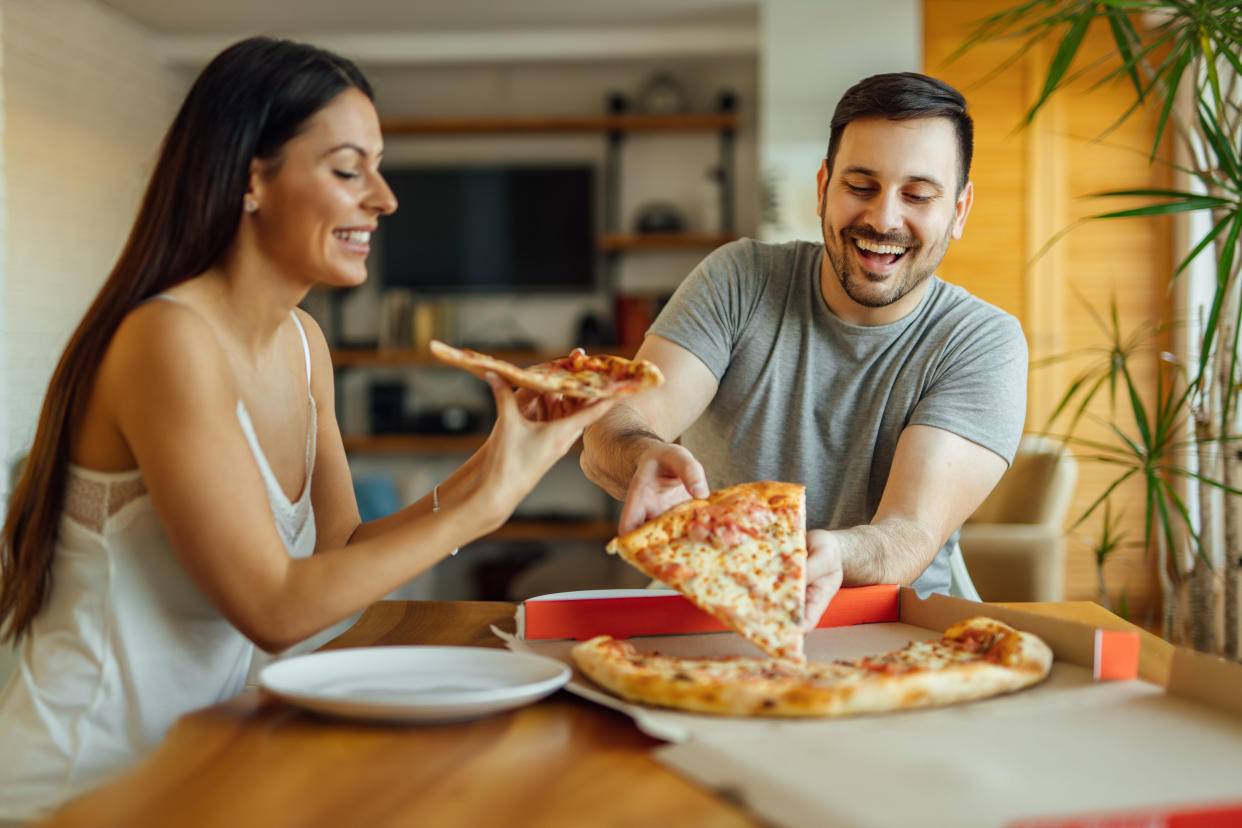 Pizza for breakfast? Why not! Cheerful couple in pajamas eating pizza at home, portrait.