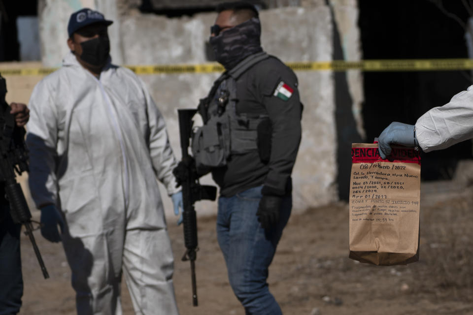 A forensic technician holds a bag of evidence collected during an excavation on a plot of land referred to as a cartel "extermination site" where burned human remains are buried, on the outskirts of Nuevo Laredo, Mexico, Tuesday, Feb. 8, 2022. Each day, technicians place what they find -- bones, buttons, earrings, scraps of clothing -- in paper bags labeled with their contents and send them off to the forensic lab in the state capital Ciudad Victoria. (AP Photo/Marco Ugarte)