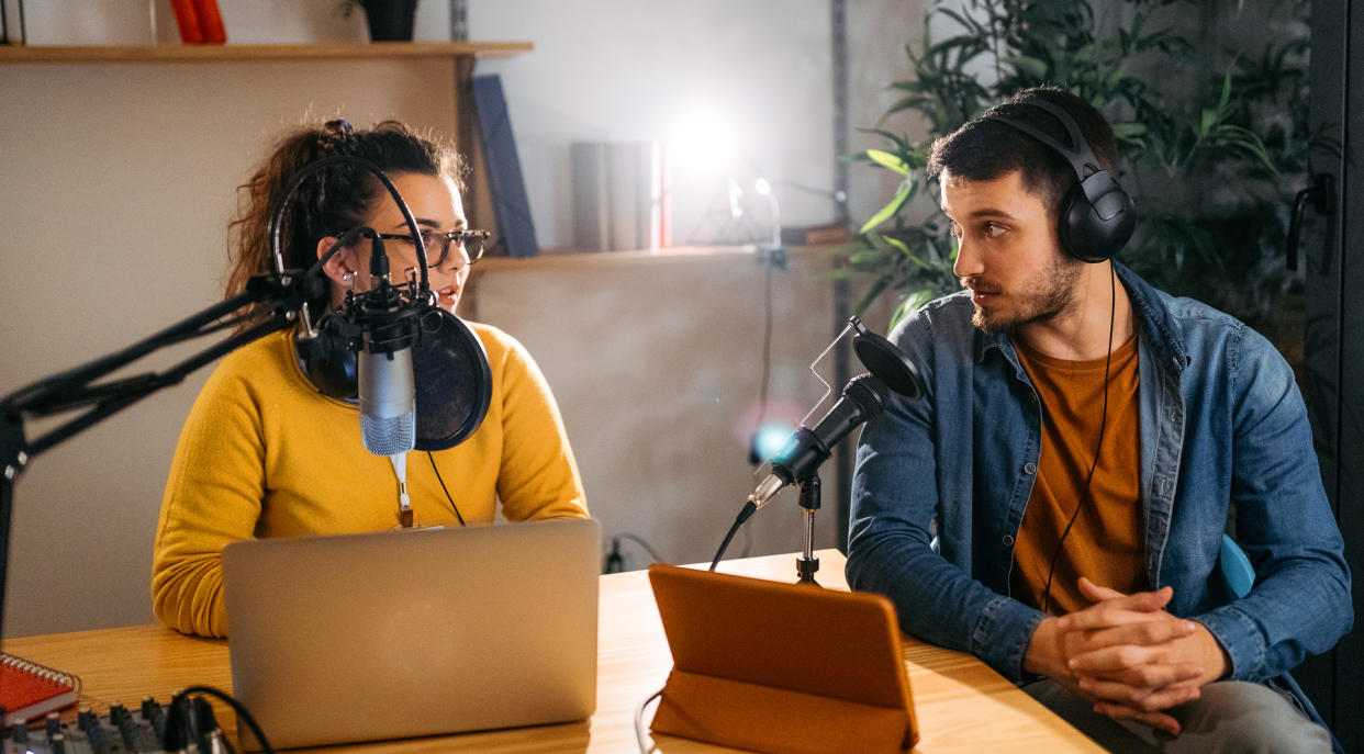  two people recording a podcast, with a laptop and an ipad and some microphones 