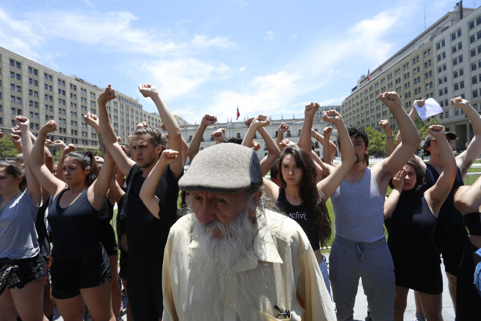 An elderly man walks in front of theater students performing in support of demonstrators who suffered eye injuries during the ongoing anti-government protests, in front of the Palacio de La Moneda, in Santiago, Chile, Friday, Dec. 13, 2019. The demonstrators claim that their injuries are the result of being shot with shotguns by the police. The United Nations released on Friday a lapidary report which stated that there have been serious violations of human rights during the repression of recent protests in Chile. (AP Photo/Luis Hidalgo)