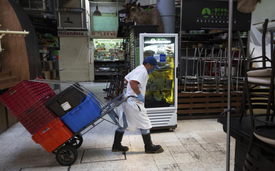 An employee wearing a protective face mask and disposable gloves, hauls crates with the aid of a trolley through the popular and normally crowded San Juan food market, in Mexico City, Wednesday, March 25, 2020. Mexico's capital has shut down museums, bars, gyms, churches, theaters, and other non-essential businesses that gather large numbers of people, in an attempt to slow the spread of the new coronavirus. (AP Photo/Fernando Llano)