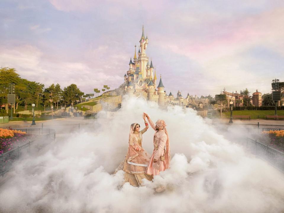 A groom twirls a bride surrounded by fog in front of Cinderella's castle at Disneyland Paris.