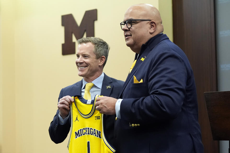 Dusty May, left, is presented a Michigan jersey by Athletic Director Warde Manuel before being introduced as the new Universtiy of Michigan NCAA college basketball head coach, Tuesday, March 26, 2024, in Ann Arbor, Mich. (AP Photo/Carlos Osorio)