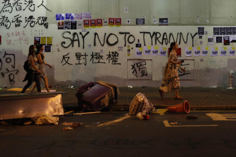 People walk past a wall with graffiti in Hong Kong, Sunday, Sept. 29, 2019. Protesters and police clashed in Hong Kong for a second straight day on Sunday, throwing the city's business and shopping belt into chaos and sparking fears of more ugly scenes leading up to China's National Day this week. (AP Photo/Gemunu Amarasinghe)