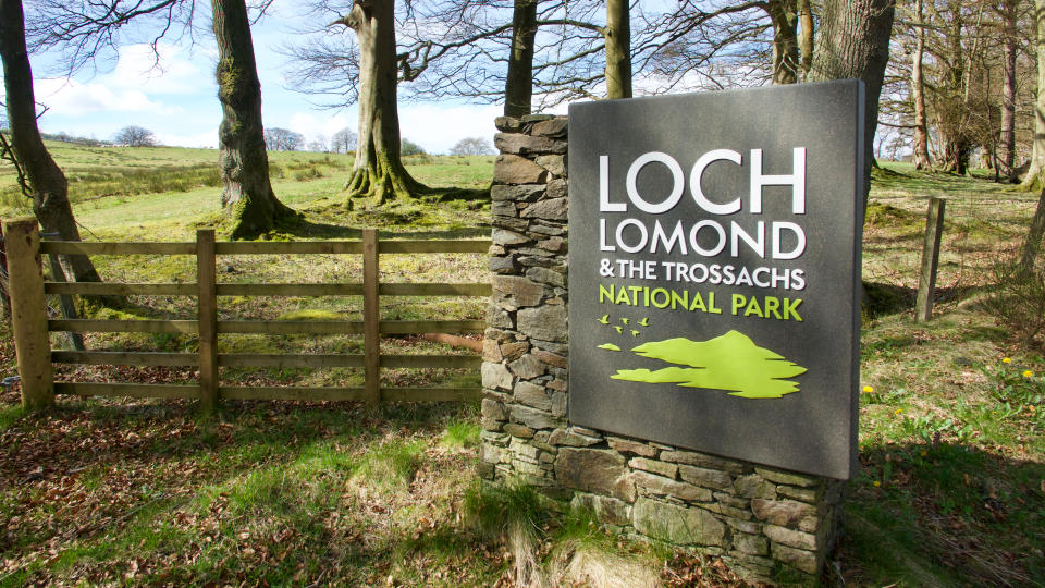 Sign at the roadside near Croftamie with wooden fence, trees and field in the background.