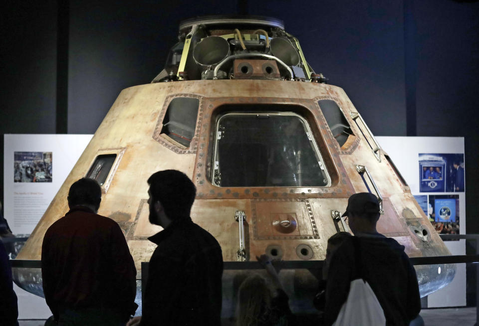 Visitors look at the NASA Apollo 11 command module Columbia, the centerpiece of Destination Moon: The Apollo 11 Mission exhibit at the Museum of Flight, Friday, July 19, 2019, in Seattle. The module functioned as a mother ship, carrying the crew of three astronauts and the second Apollo spacecraft, the lunar module, to orbit around the moon, and brought the astronauts back to Earth. The exhibit commemorates the historic landing by American astronauts on the moon 50 years earlier, on July 20, 1969. (AP Photo/Elaine Thompson)