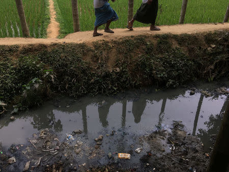 Two men walk between a rice field and a trash-choked canal running alongside the Rohingya shacks set up on the land of Bangladeshi farmer Jorina Katun near the Kutapalong refugee camp in the Cox's Bazar district of Bangladesh February 9, 2018. Picture taken February 9, 2018. REUTERS/Andrew RC Marshall