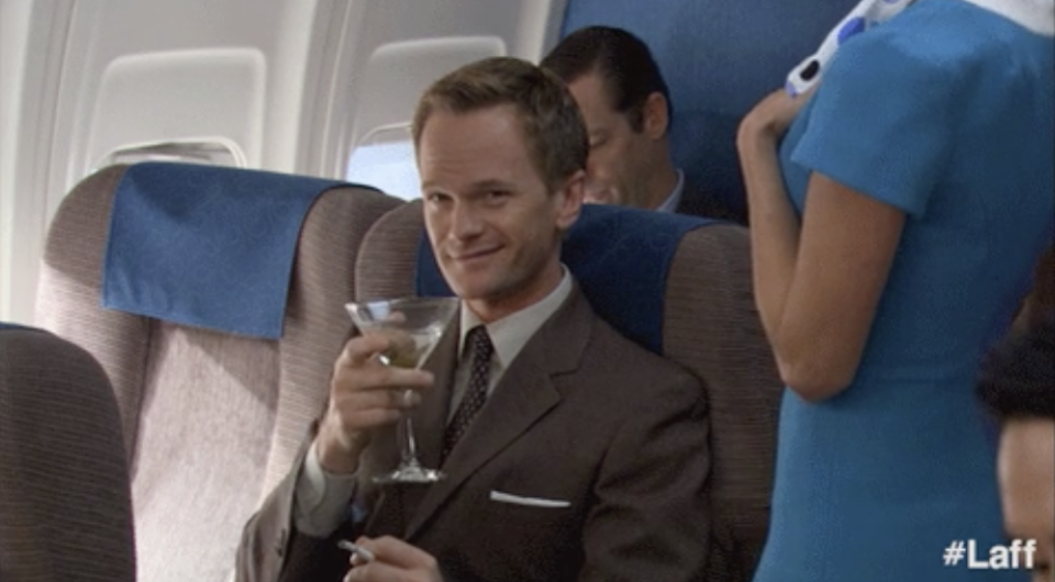 a man winking drinking a martini on an airplane