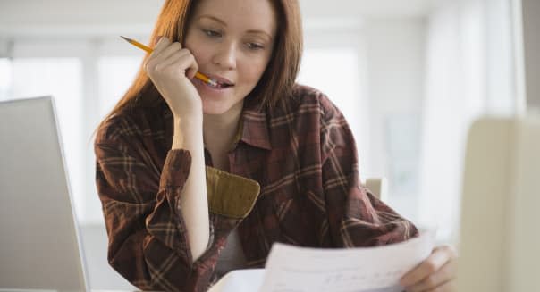 Woman biting on pencil while looking at bills