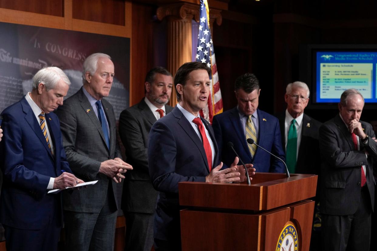 Republican Sen. Ben Sasse of Nebraska, his hands perched atop a podium, is surrounded by a half-dozen GOP colleagues while addressing reporters at a press conference in the US Capitol.