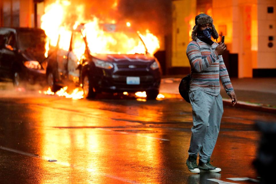 A person holds a phone and stands in front of burning vehicles following demonstrations protesting the death of George Floyd, a black man who died May 25 in the custody of Minneapolis Police, in Seattle, Washington on May 30, 2020.