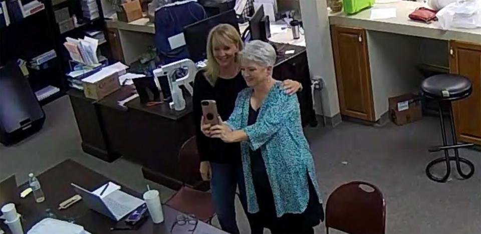 A view from above of Cathy Latham posing with another woman and taking a selfie inside an office