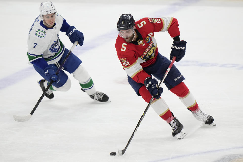 Florida Panthers defenseman Aaron Ekblad (5) passes the puck as he is guarded by Vancouver Canucks right wing William Lockwood (7) during the second period of an NHL hockey game, Saturday, Jan. 14, 2023, in Sunrise, Fla. (AP Photo/Wilfredo Lee)