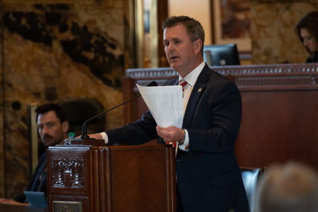 Representative Beau Beaullieu at a podium with a microphone. He holds a piece of paper in his hands.