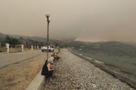 People sit on the beach as a wildfire approaches Limni village on the island of Evia, about 160 kilometers (100 miles) north of Athens, Greece, Friday, Aug. 6, 2021. Thousands of people fled wildfires burning out of control in Greece and Turkey on Friday, including a major blaze just north of the Greek capital of Athens that claimed one life, as a protracted heat wave left forests tinder-dry and flames threatened populated areas and electricity installations. (AP Photo/Thodoris Nikolaou)