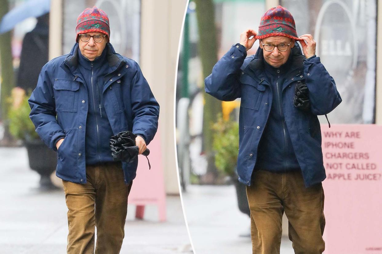 Rick Moranis in New York City, wearing a hat and jacket on a rainy day.
