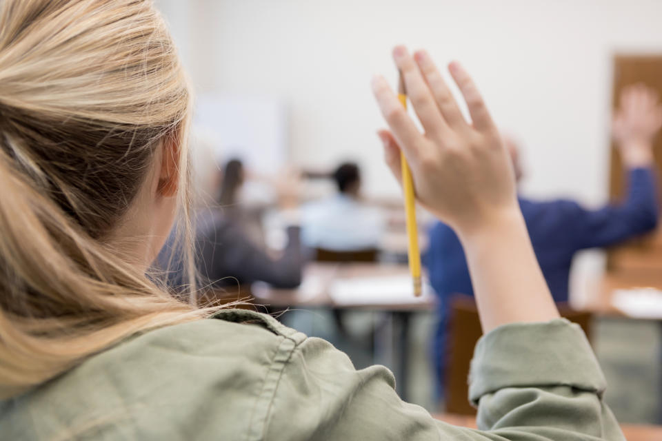 Person raising hand in a classroom setting, indicating participation or a question