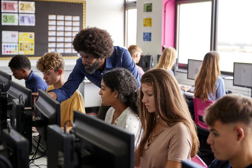 Male Teacher Helping Teenage Female High School Student Working In Computer Class