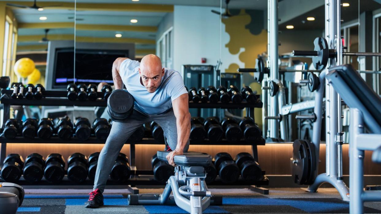  Man performs one-arm dumbbell row in gym. 