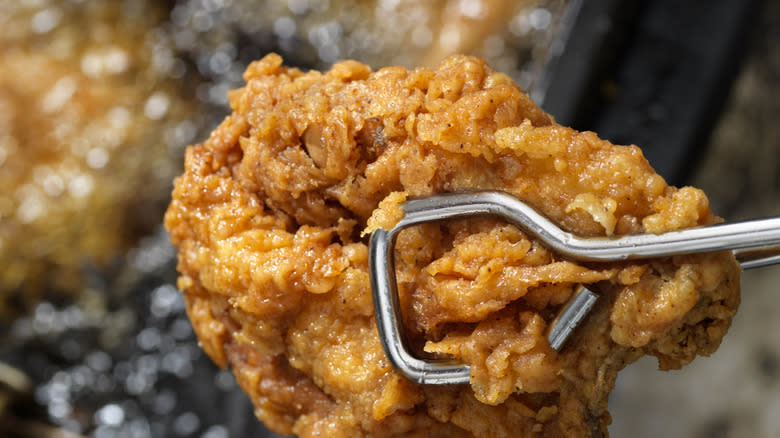 Tongs holding fried chicken