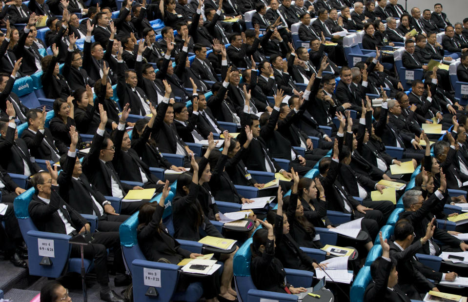 In this Wednesday, June 5, 2019 photo, members of the parliament representing military-backed Palang Pracharath party raise their hands approving the nomination of Prayuth Chan-ocha as Thailand's Prime Minister in Bangkok, Thailand. A Thai court said Wednesday, June 26 it will allow 32 pro-military lawmakers to keep their seats while it decides whether they violated election rules by holding shares in media companies, a decision criticized as unfair because the court earlier suspended the leader of the anti-military Future Forward Party, Thanathorn Juangroongruangkit, over a similar allegation. (AP Photo/Gemunu Amarasinghe)