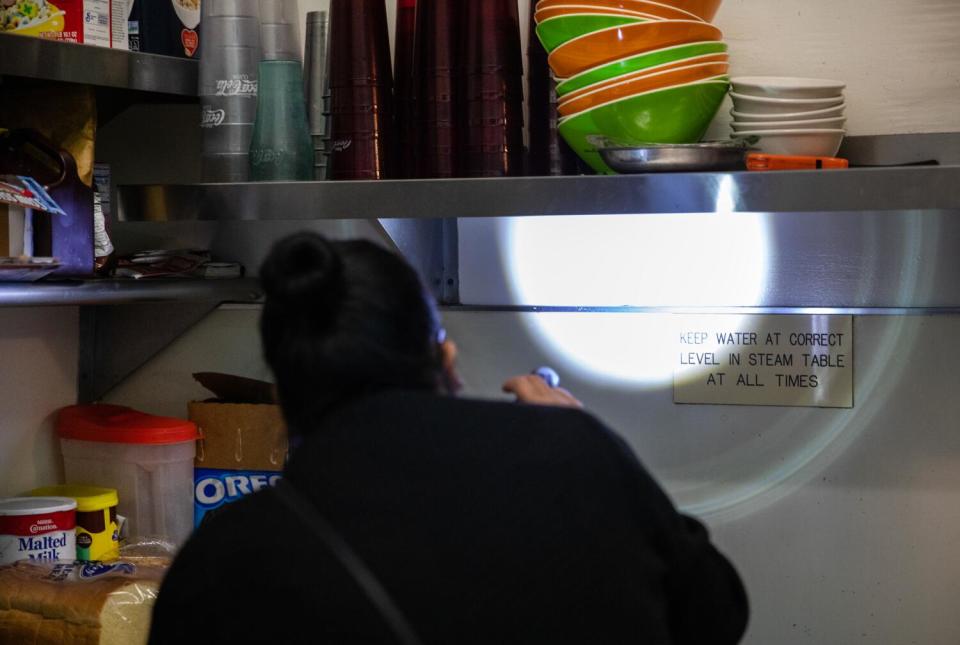 McShane uses a flashlight to inspect shelving and make sure there are no vermin present at the Great Grill.