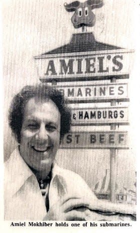 From 1976, Amiel J. Mokhiber Sr. holds one of his submarine sandwiches in front of an Amiel’s Original Submarines shop.