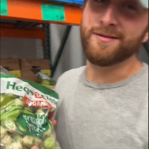 A person holds a bag of organic Brussels sprouts in a grocery store aisle