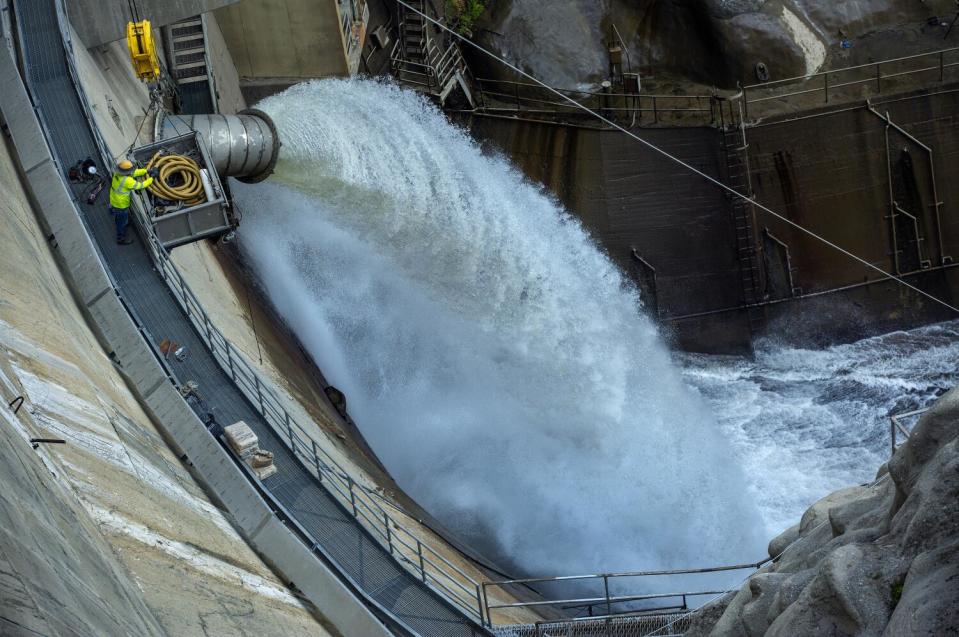 Water spews from a massive pipe along the wall of a dam.