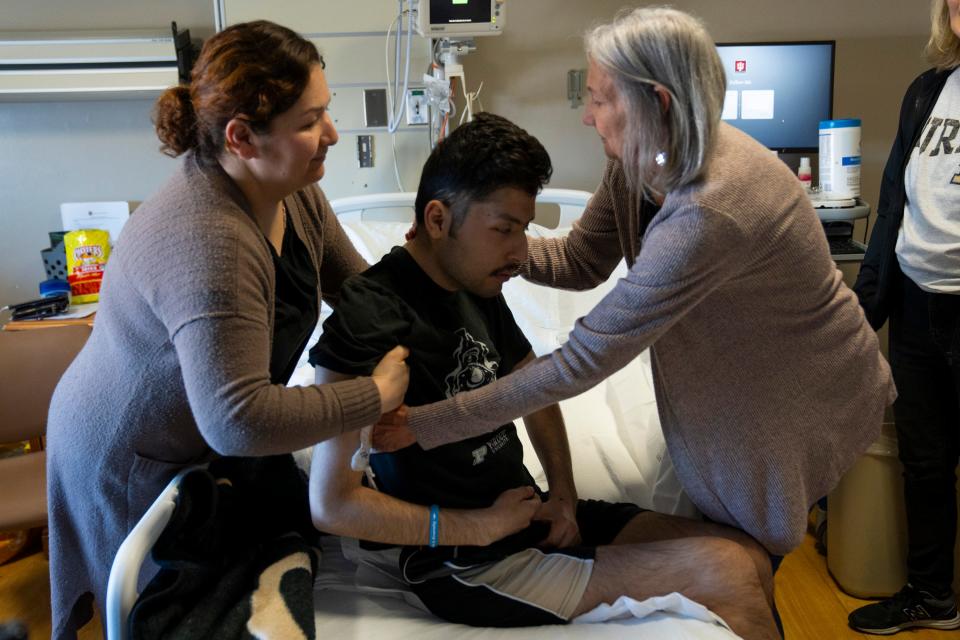 Jonathan Avalos, middle, is helped out of bed by Maria Avalos, his mother, left, and Diana Boswell, a nurse, to watch the Purdue Boilermakers play NC State in the NCAA Men’s Basketball Tournament Final Four game with his mother, sister, cousin and best friends, Saturday, April 6, 2024, in the B5 Comfort Care unit at the IU Health Methodist Hospital in Indianapolis. Avalos is a 22-year-old Purdue student with glioblastoma, an incurable type of primary brain cancer.