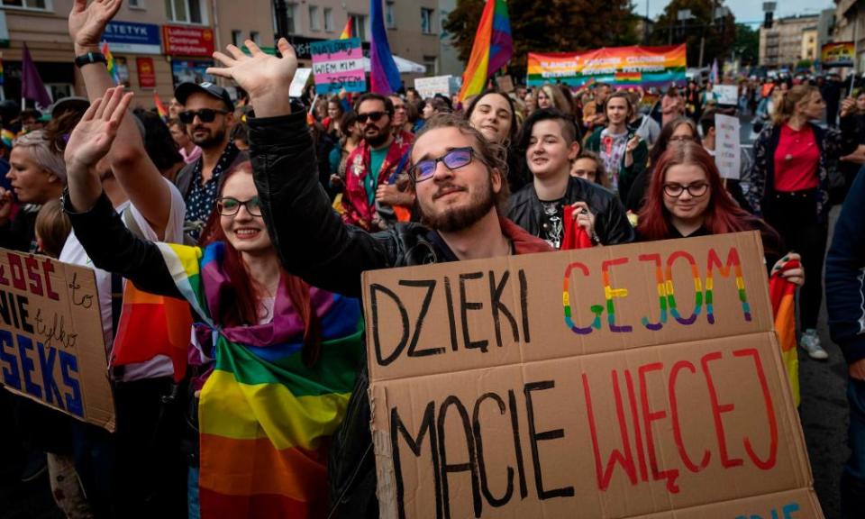 A crowd of people march with rainbow flags and colourful signs