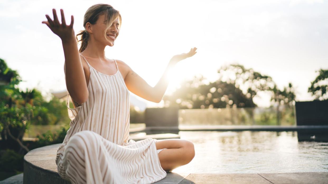 mujer sonriente haciendo yoga y meditación junto a una piscina 