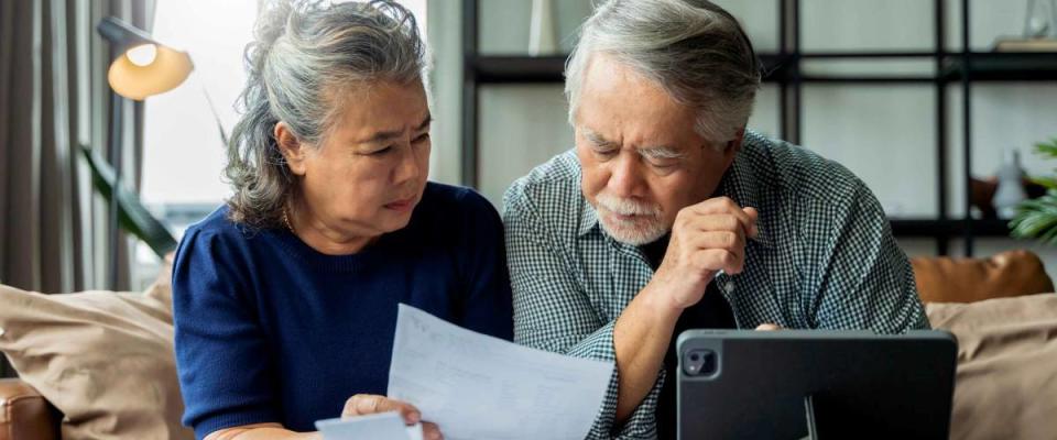 senior couple checking bills together on sofa, looking concerned.